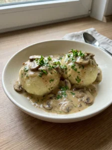 Ein tiefer Teller mit zwei Kartoffelknödeln, übergossen mit einer hellen Soße mit Pilzstücken.
