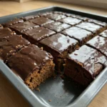 Rechteckige Stücke von Lebkuchen mit dunklem Schokoguss auf einem Backblech.