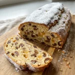 Ein ganzer Quarkstollen, dick mit Puderzucker bestäubt, auf einem Holzbrett.