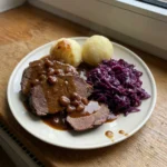 Aufgeschnittener Sauerbraten auf einem Teller mit Klößen, Rotkohl und der dunklen Soße.