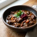 Ein tiefer Teller mit Wildgulasch in dunkler Sauce, garniert mit Petersilie.